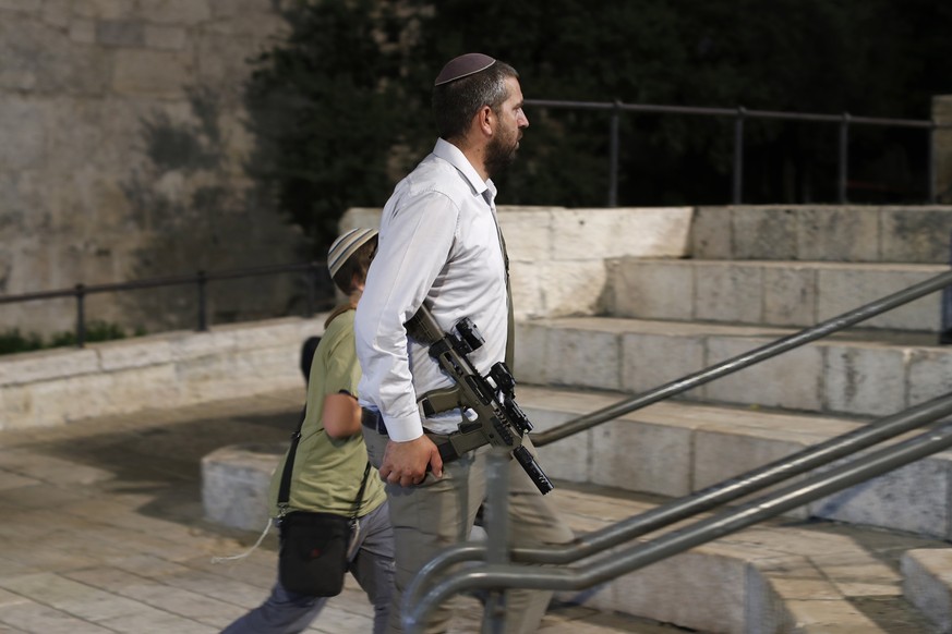 epa10770343 An armed Jewish settler walks near the Damascus Gate of Jerusalem's Old City during a right-wing march on his way to attend a special prayer at the Western Wall on the eve of Tisha B'o...