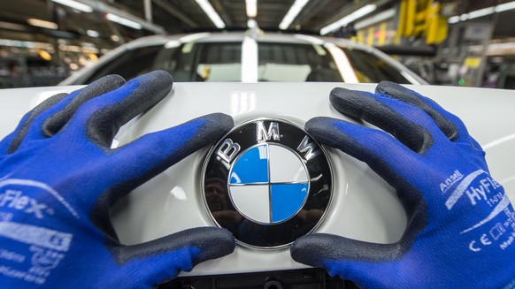 ARCHIV - 04.12.2015, Bayern, Dingolfing: Ein Mitarbeiter montiert im BMW-Werk ein BMW-Emblem auf den Kofferraumdeckel eines Fahrzeugs der 7er Reihe. BMW praesentiert am 21.03.2018 die Bilanz. (KEYSTON ...