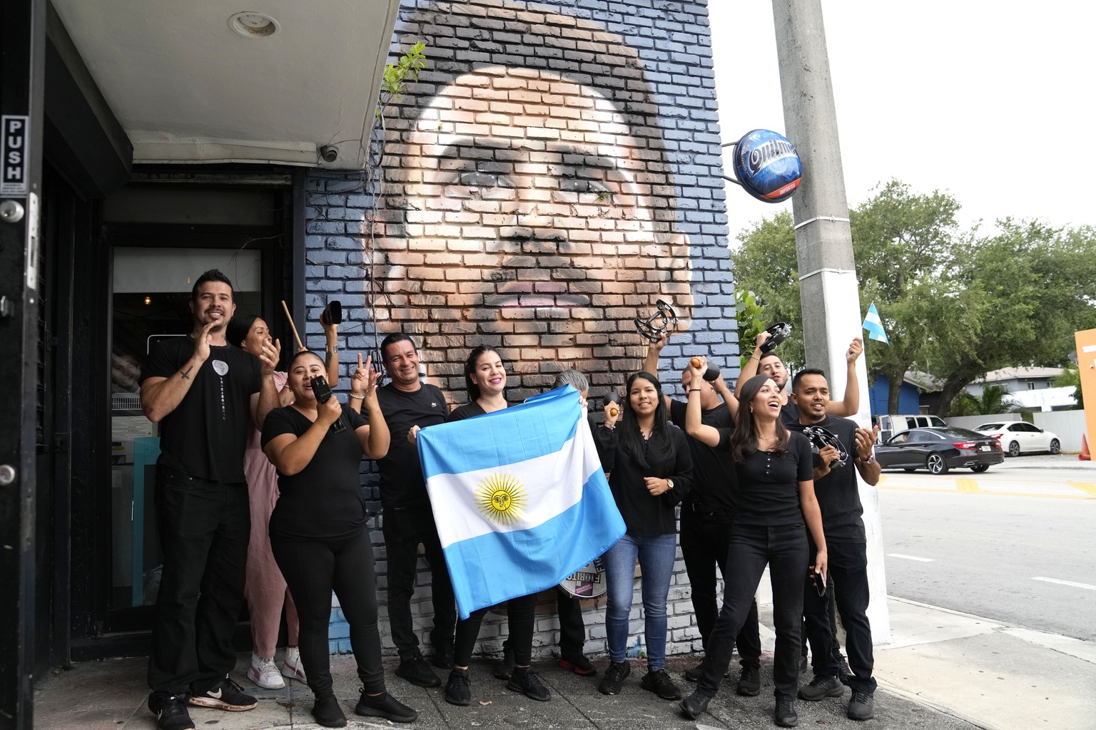 Staff at the Fiorito restaurant hold an Argentinian flag as they pose for a photograph taken by a colleague in front of a mural of Lionel Messi, Wednesday, June 7, 2023, in Miami. The Argentine soccer ...