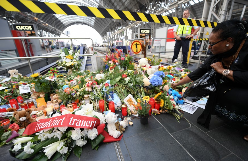 31.07.2019, Hessen, Frankfurt/Main: Eine Frau legt am Gleis 7 des Hauptbahnhofs Blumen ab, im Vordergrund liegt eine Schleife mit der Aufschrift &quot;Frankfurt trauert&quot;. Ein achtjähriger Junge w ...