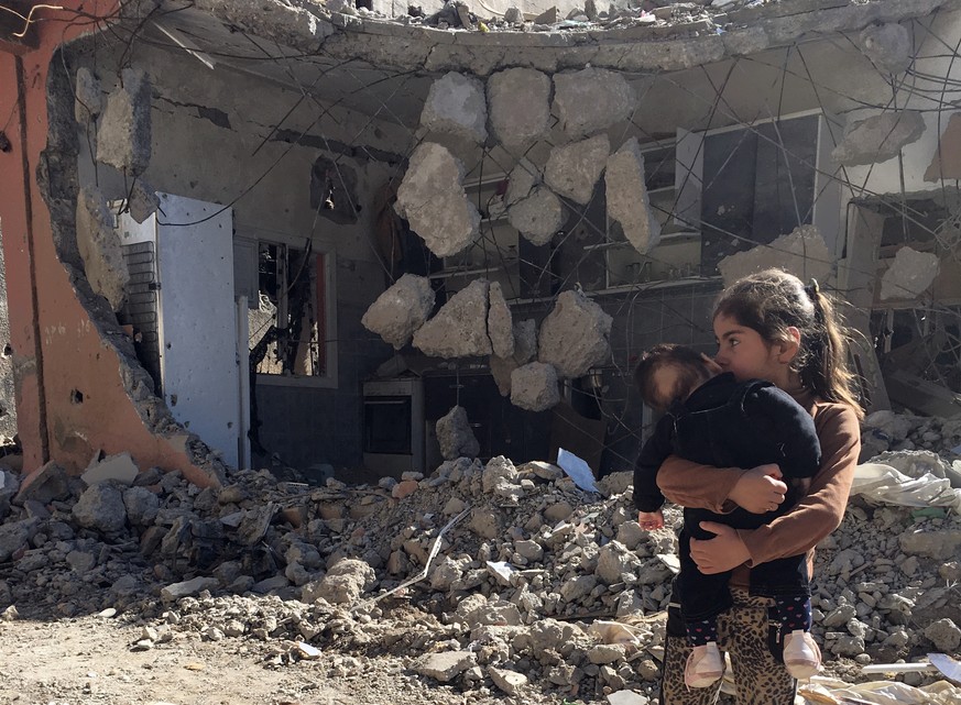 A young girl holds a child in front of a ruined house in Cizre, Turkey, Wednesday, March 2, 2016. Turkish authorities on Wednesday scaled down a 24-hour curfew imposed on the mainly Kurdish town of Ci ...