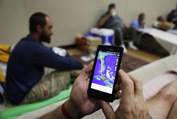 Tim Grollimund looks at the projected path of Hurricane Irma on his phone while staying in a shelter in Miami after evacuating his home in Key Largo along the Florida Keys, Saturday, Sept. 9, 2017. (A ...