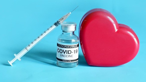 Coronavirus COVID-19 Vaccine Glass Bottle, syringe and Heart-shaped plastic box isolated on blue background with copy space at Thailand. Medical device concept. Selective Focus.