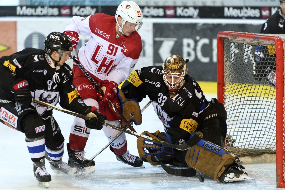 L'attaquant fribourgeois Nathan Marchon, gauche, et le gardien Fribourgeois Barry Brust, droite, luttent pour le puck avec l'attaquant lausannois Joel Vermin, centre, lors de la rencontre du ...