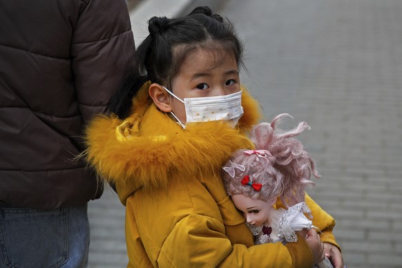 A child wearing a face mask to help curb the spread of the coronavirus holds a doll as she heads to her kindergarten in Beijing, Wednesday, March 17, 2021. (AP Photo/Andy Wong)