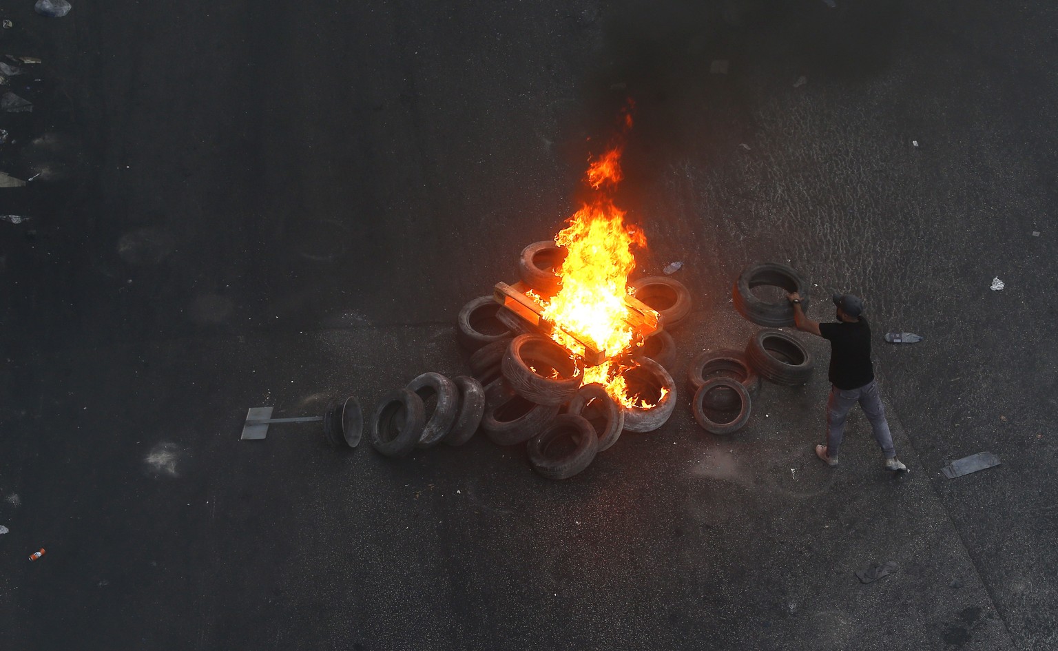 epa10726409 A Palestinian man throws tyres in a fire during clashes with the Israeli army on the second day of a military operation in Jenin camp, West Bank, 04 July 2023. The Israeli army stated on 0 ...