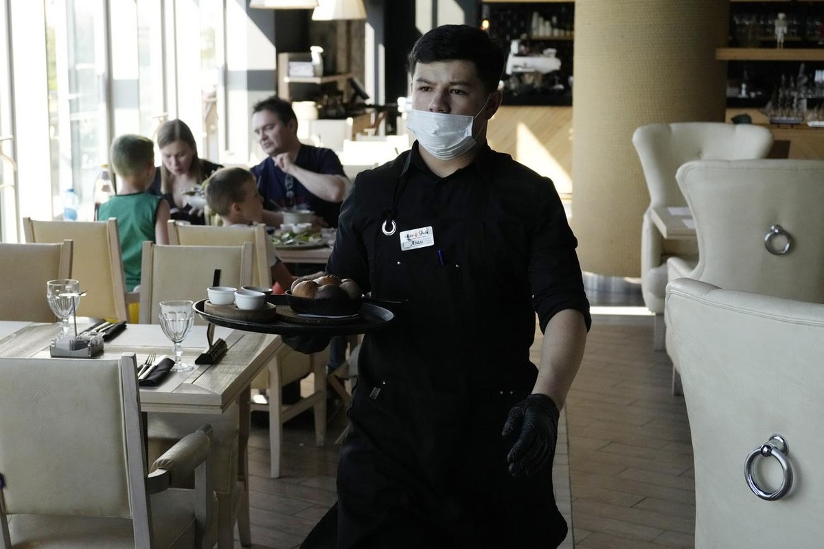 A waiter wearing a face mask and gloves to protect against coronavirus, serve customers in a restaurant "Meat and fish" in Moscow, Russia, Friday, June 18, 2021. As coronavirus cases rise dr ...