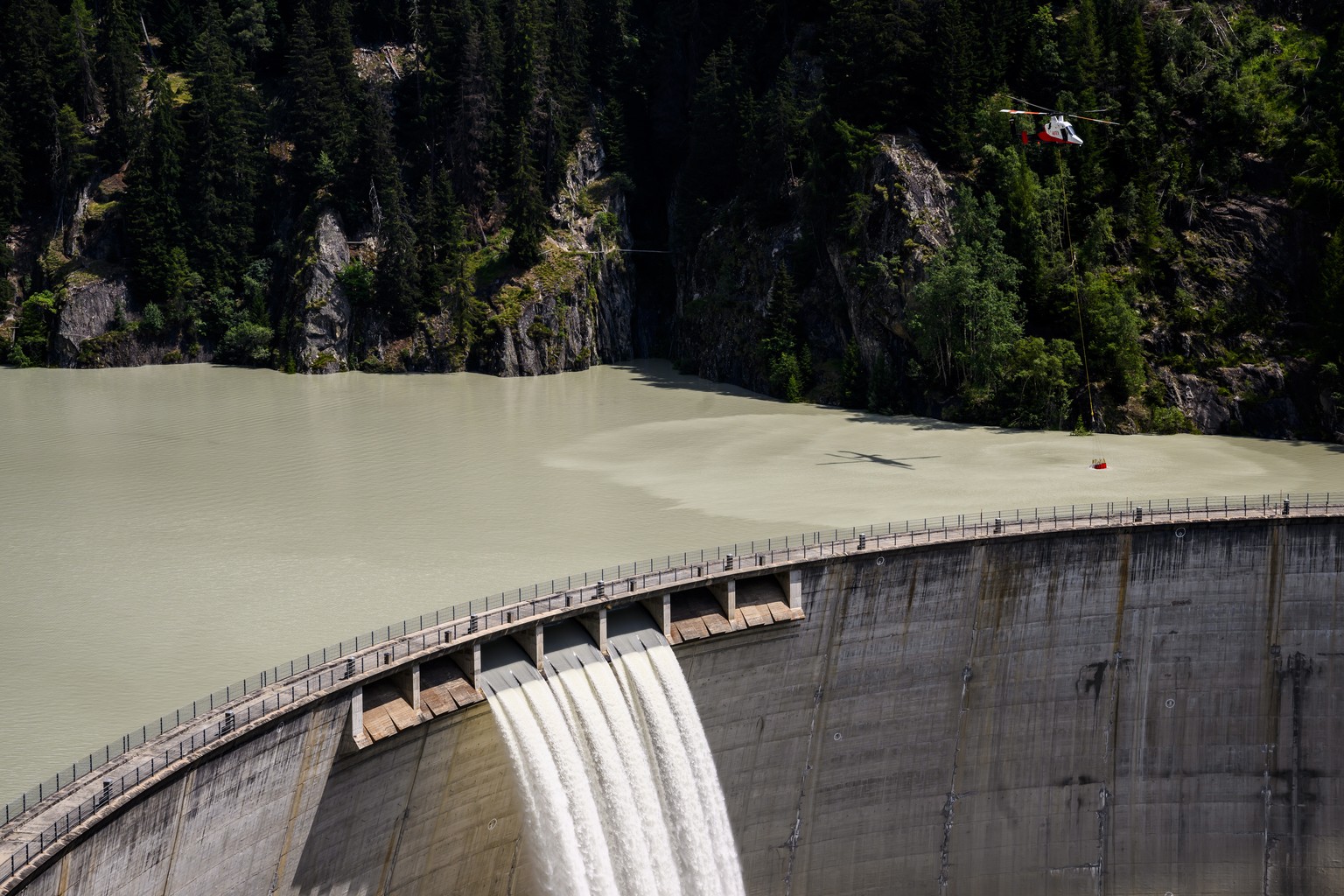 epa10753310 A Rotex helicopter refills its bucket with water over Gibidum dam to extinguish forest fire above the communes of Bitsch and Ried-Moerel, in Naters, Switzerland, 18 July 2023. A forest fir ...