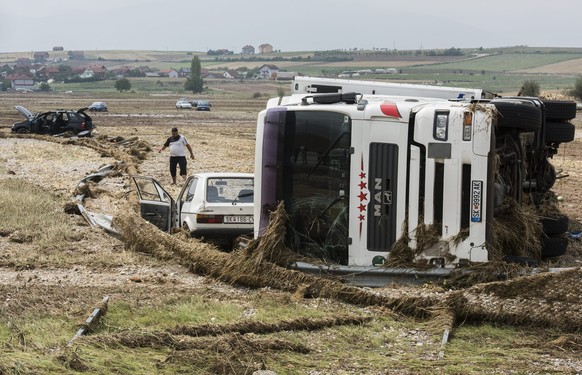 epa05461016 A man walks between vehicles which were swept in to a field near the ring road around Skopje, The Former Yugoslav Republic of Macedonia on 07 August 2016. At least 15 people have died in a ...