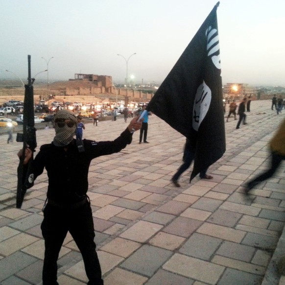 A fighter of the Islamic State of Iraq and the Levant (ISIL) holds an ISIL flag and a weapon on a street in the city of Mosul June 23, 2014. To match Exclusive MIDEAST-CRISIS/IRAQ-MOSUL REUTERS/String ...