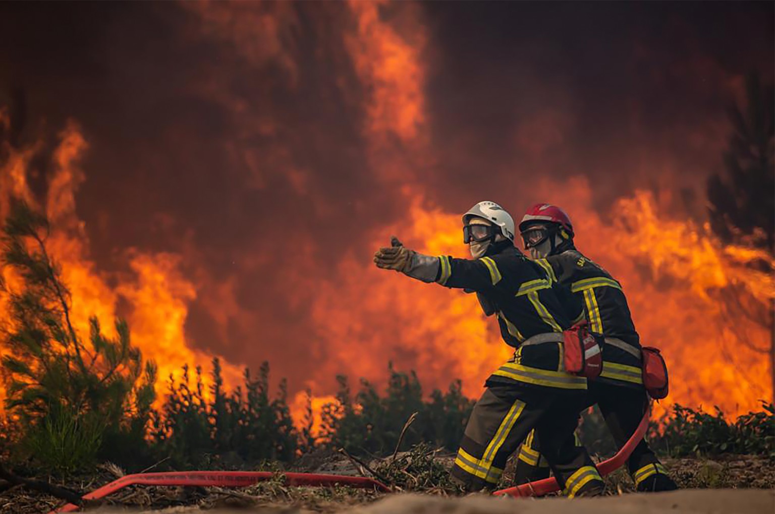 This photo provided by the fire brigade of the Gironde region (SDIS 33) shows firefighters unroll the fire hose at a forest fire at La Test-de-Buch, southwestern France, late Monday, July 18, 2022. Fr ...