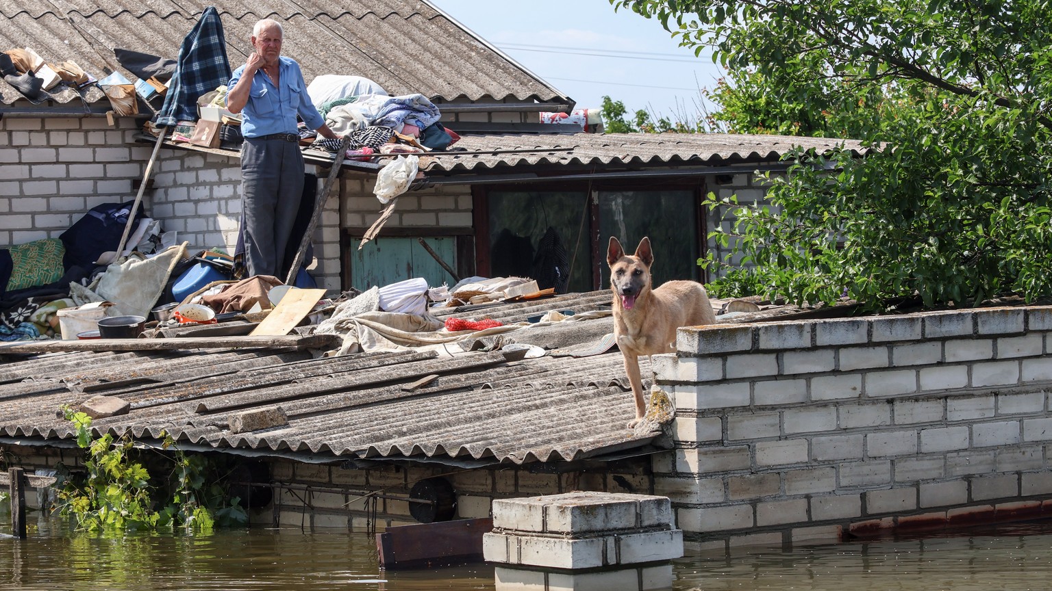 epa10681888 A local resident on the roof of his house in the flooded area of Kherson, Ukraine, 09 June 2023. Ukraine has accused Russian forces of destroying a critical dam and hydroelectric power pla ...