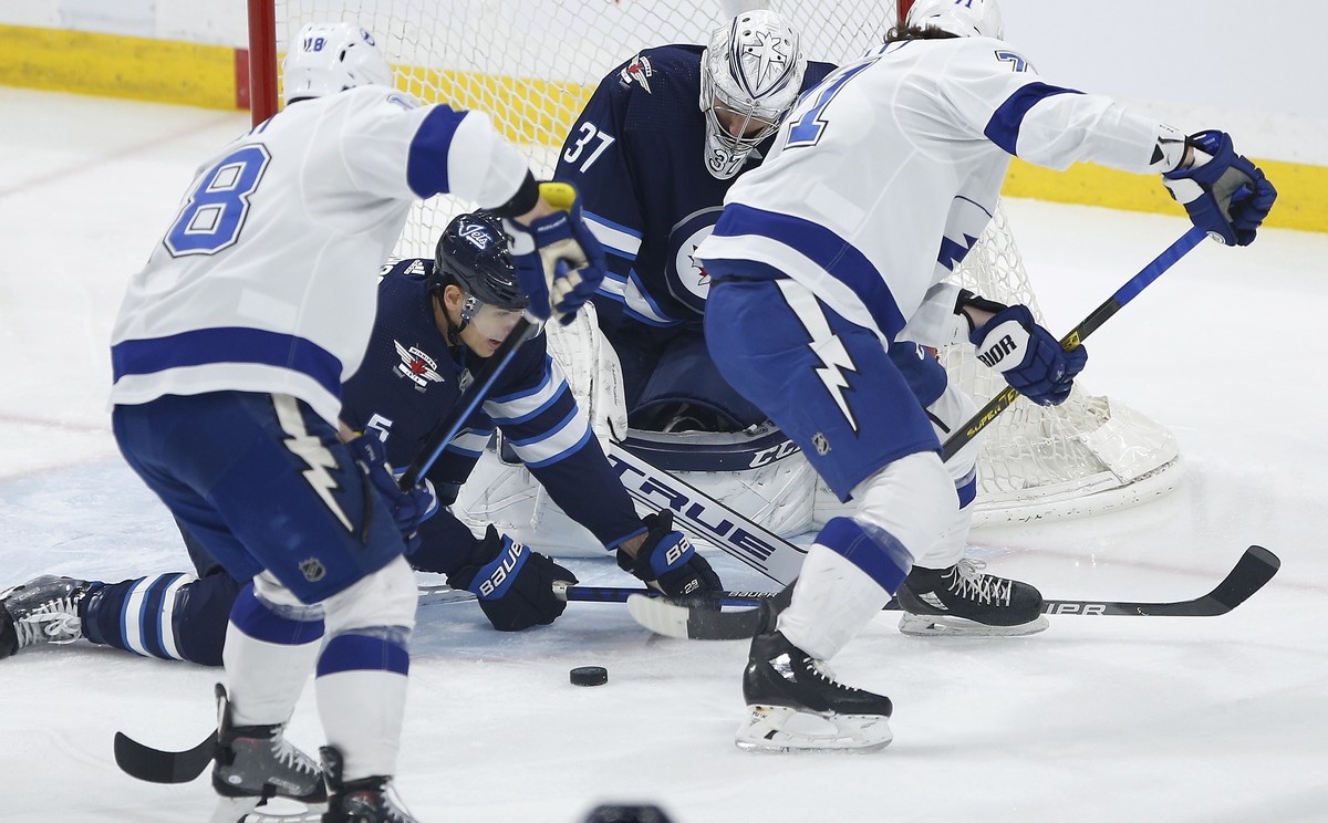 Winnipeg Jets goaltender Connor Hellebuyck (37) watches the puck Tampa Bay Lightning's Ondrej Palat (18) and Anthony Cirelli (71) look for the rebound and Jets' Luca Sbisa (5) defends during ...