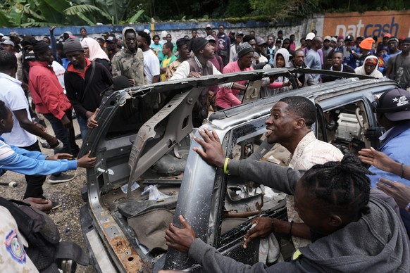 Residents try to flip over a car to block a street as they protest for police intervention after deadly gang attacks in the Kenscoff neighborhood of Port-au-Prince, Haiti, Monday, Aug. 24, 2026. (AP P ...