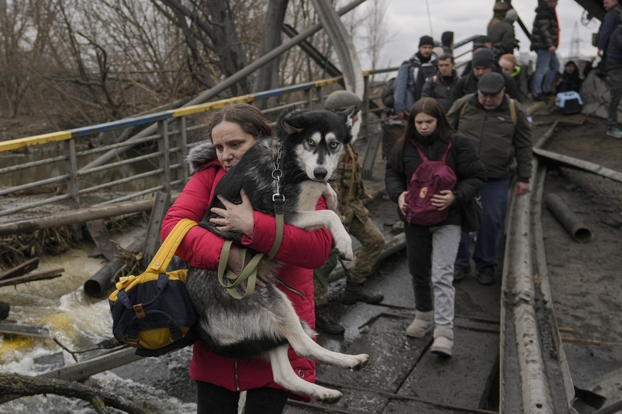 A woman holds a dog while crossing the Irpin River on an improvised path under a bridge that was destroyed by a Russian airstrike, while assisting people fleeing the town of Irpin, Ukraine, Saturday,  ...