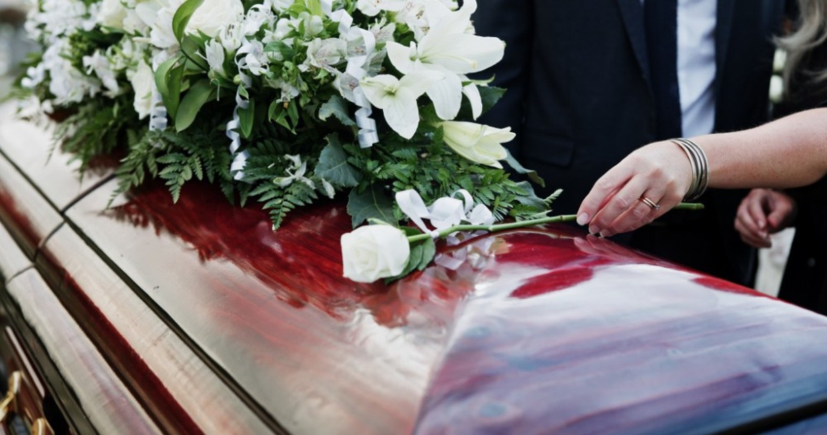 Woman, hand and rose in cemetery with coffin, funeral service and people mourning for burial ceremony. Person, white flower and casket in graveyard outdoor with memorial, family death or bereavement.