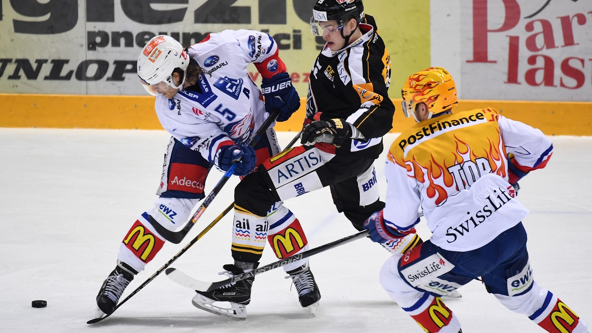 Zurich's player Severin Blindenbacher, left, fights for the puck with Lugano’s player Gregory Hofmann, center, during the second leg of the Playoffs quarterfinals game of National League A (NLA)  ...