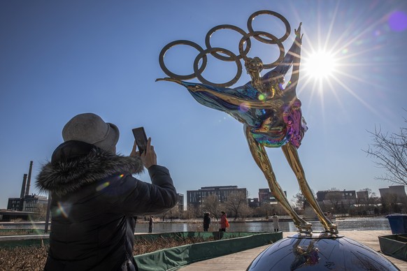 epa09614026 A woman takes photos with her mobile phone of a figure skating sculpture erected for the Beijing 2022 Winter Olympics, at the Shougang Industrial Park, which will be used as a venue for ho ...