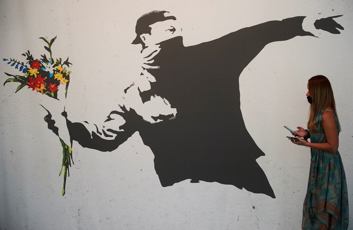 epa09578522 A woman walks past a reproduction of the work 'Rage Flower Thrower' by British anonymous street artist Banksy, on display in the exhibition 'Banksy. The Art of Protest' ...