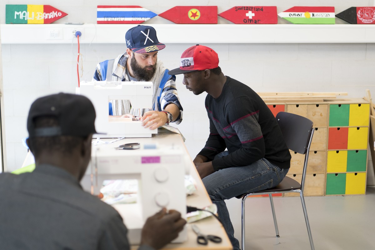 Un employe de ORS Encadrement, centre, explique le fonctionnement d'une machine a coudre a deux refugies lors des portes ouvertes du Centre federal pour requerants d'asile, CFA, ce samedi 1  ...