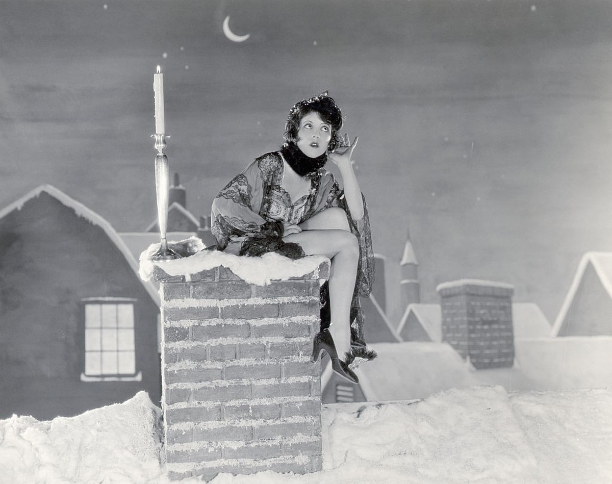 (Original Caption) Actress Clara Bow sits on a chimney with a candle listening for the arrival of Santa Claus in and unidentified Paramount Pictures' film. Undated movie still.