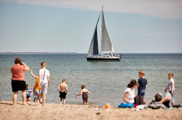 09.05.2021, Schleswig-Holstein, Scharbeutz: Menschen genie�en das sonnige und warme Wetter am Sonntagnachmittag an einem Strand der L�becker Bucht, w�hrend ein Segelboot vorbeif�hrt. Seit Samstag, 8.  ...