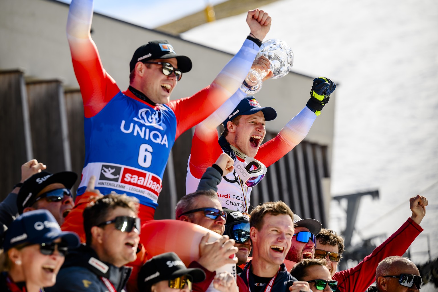 The winner of the race Stefan Rogentin of Switzerland, left and Marco Odermatt of Switzerland, right, with the men&#039;s super-g overall leader crystal globe trophy, celebrate with Swiss-ski team&#03 ...