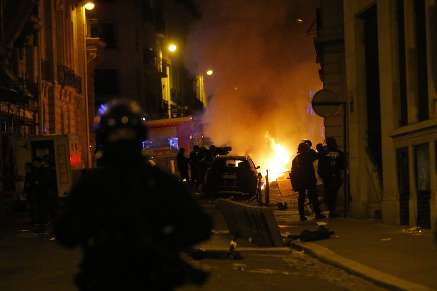 French police officers watch a car burning near the Champs-Elysee avenue following incidents after the Champions League soccer final match between PSG and Bayern Munich which is played in Lisbon, Port ...