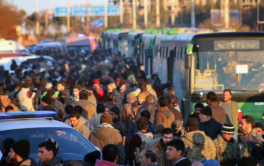 FILE - This file image released on Thursday, Dec. 15, 2016 by Aleppo 24, shows residents gathered near green government buses as they hold their belongings for evacuation from eastern Aleppo, Syria. T ...