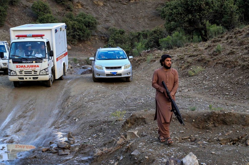 epa10028425 An armed man looks walks by as an ambulance shift victims of earthquake in Gayan village in Paktia province, Afghanistan, 22 June 2022. More than 1,000 people were killed and over 1,500 ot ...