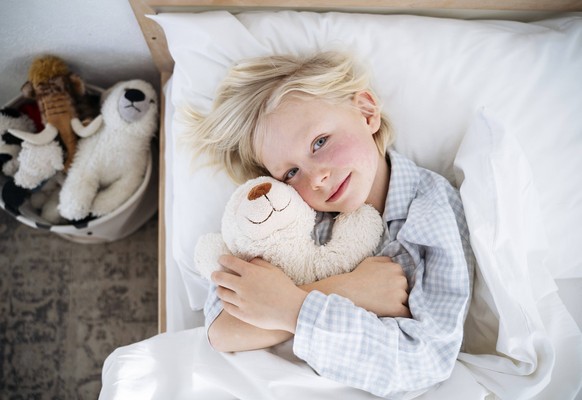 Smiling boy lying down with teddy bear on bed at home model released, Symbolfoto property released, NJAF00765