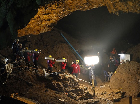 epa06853964 Thai officials carry oxygen tanks through a cave complex during a rescue operation for a missing football team at the Tham Luang cave in Tham Luang Khun Nam Nang Noon Forest Park in Chiang ...