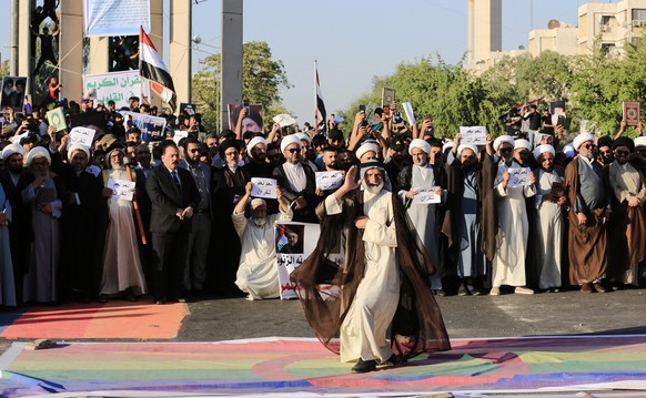 epa10719876 An Iraqi demonstrator steps over a rainbow flag, symbol of the international LGBT community, as others carry copies of the Koran during a protest near the Swedish embassy in Baghdad, Iraq, ...