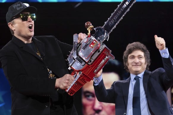Elon Musk holds up a chainsaw he received from Argentina&#039;s President Javier Milei, right, as they arrive to speak at the Conservative Political Action Conference, CPAC, at the Gaylord National Re ...