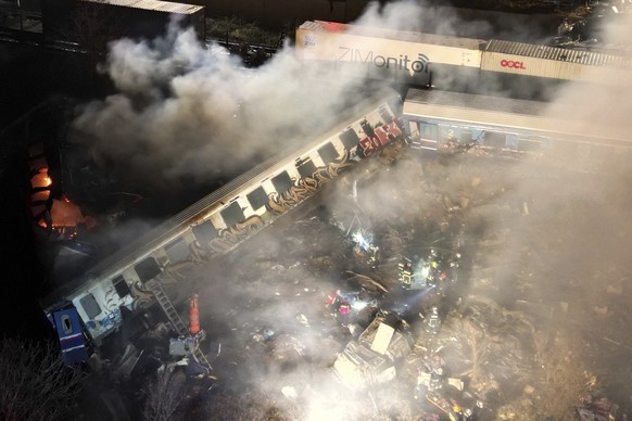 Smoke rises from trains as firefighters and rescuers operate after a collision near Larissa city, Greece, early Wednesday, March 1, 2023. The collision between a freight and passenger train occurred n ...