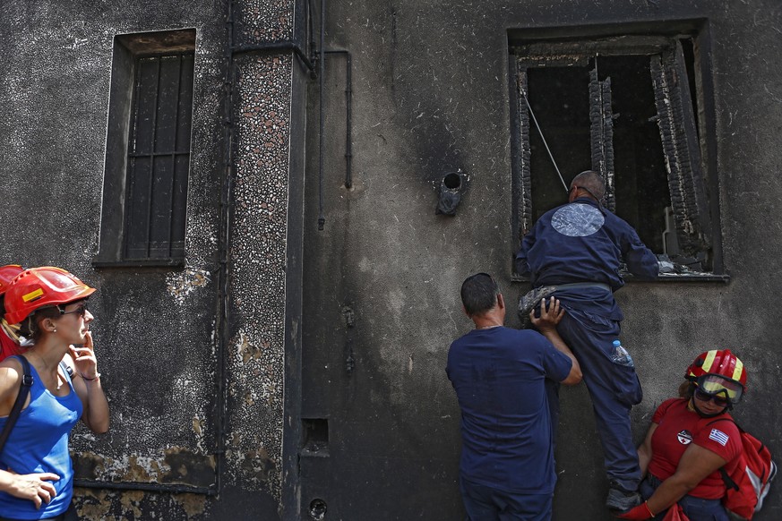 epa06909477 Members of a rescue team search for missing people inside a burned house, following a deadly forest fire in Mati a northeast suburb of Athens, Greece, 25 July 2018. The death toll from for ...