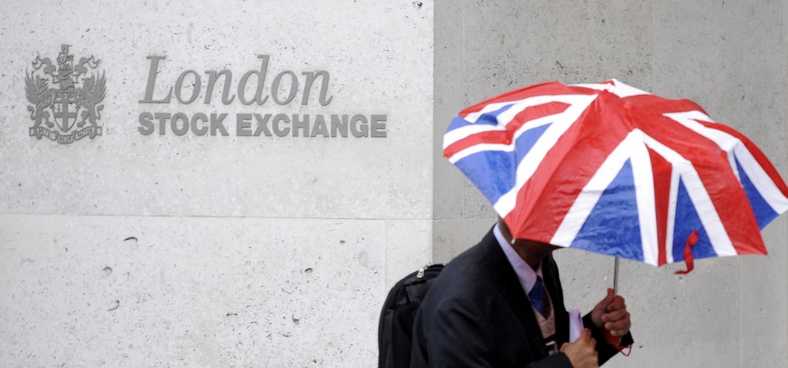 FILE PHOTO: A worker shelters from the rain under a Union Flag umbrella as he passes the London Stock Exchange in London, Britain, October 1, 2008. REUTERS/Toby Melville/File Photo