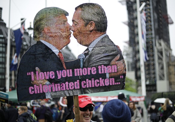 A man holds a banner depicting President Donald Trump kissing Brexit Party leader Nigel Farage during a protest against the state visit of President Donald Trump, Tuesday, June 4, 2019. Trump will tur ...