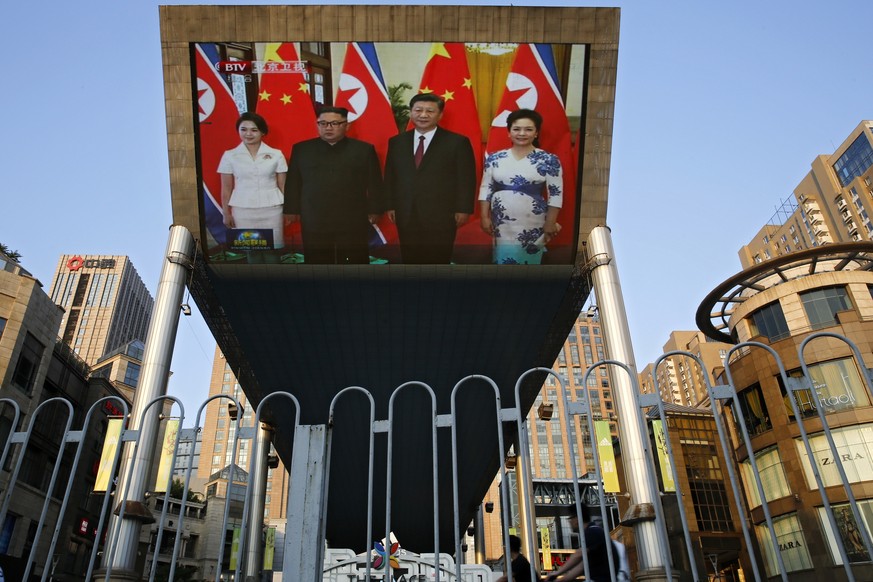 People bicycle past a giant TV screen broadcasting the meeting of visiting North Korean leader Kim Jong Un and Chinese President Xi Jinping during a welcome ceremony at the Great Hall of the People in ...