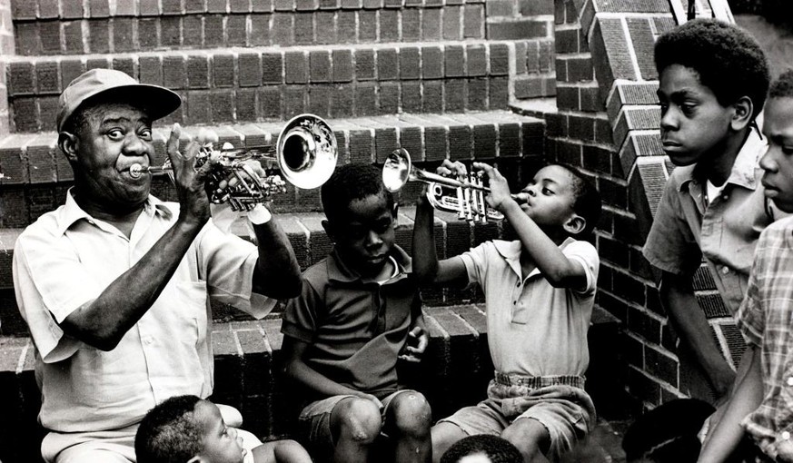 Popperfoto The Book. Volume 1. Page: 75. Picture: 21. American jazz trumpeter, band leader and singer Louis &quot;Satchmo&quot; Armstrong shows a young trumpeter and boys his art. 29th August 1970.