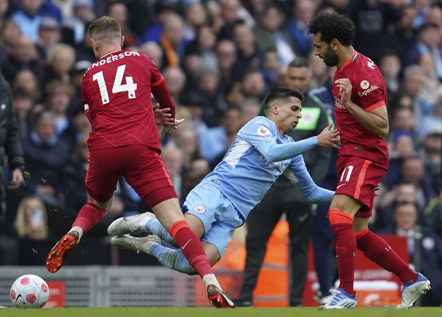 Manchester City&#039;s Joao Cancelo, center, duels for the ball with Liverpool&#039;s Jordan Henderson, left, and Liverpool&#039;s Mohamed Salah during the English Premier League soccer match between  ...