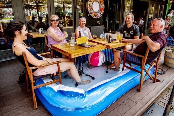 epa07739598 Tourists sit on a terrace with their feet in an inflatable swimming pool, in Amsterdam, the Netherlands, 25 July 2019. The Royal Dutch Meteorology Institute (KNMI) has issued an official w ...