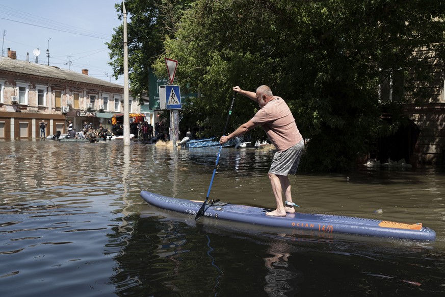 A man uses a stand-up paddleboard to reach his home in a flooded neighborhood in Kherson, Ukraine, Wednesday, June 7, 2023 after the Kakhovka Dam was blown up.  Residents Of Southern Ukraine Brace For…