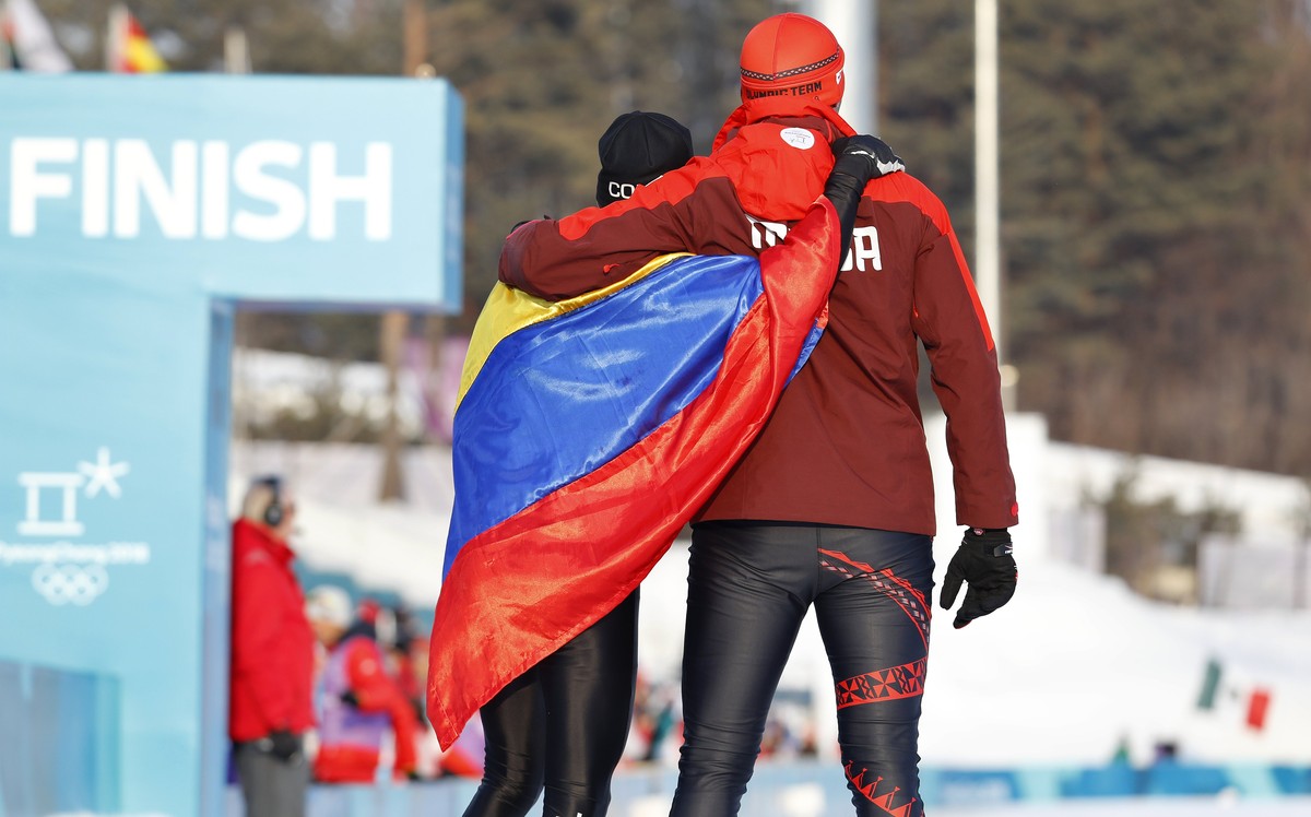 epa06531541 Pita Taufatofua (R) of Tonga and Sebastian Uprimny of Ecuador watch German Madrazo (rear) of Mexico carrying the Mexican flag and approaching the finish line in the Men's Cross Countr ...