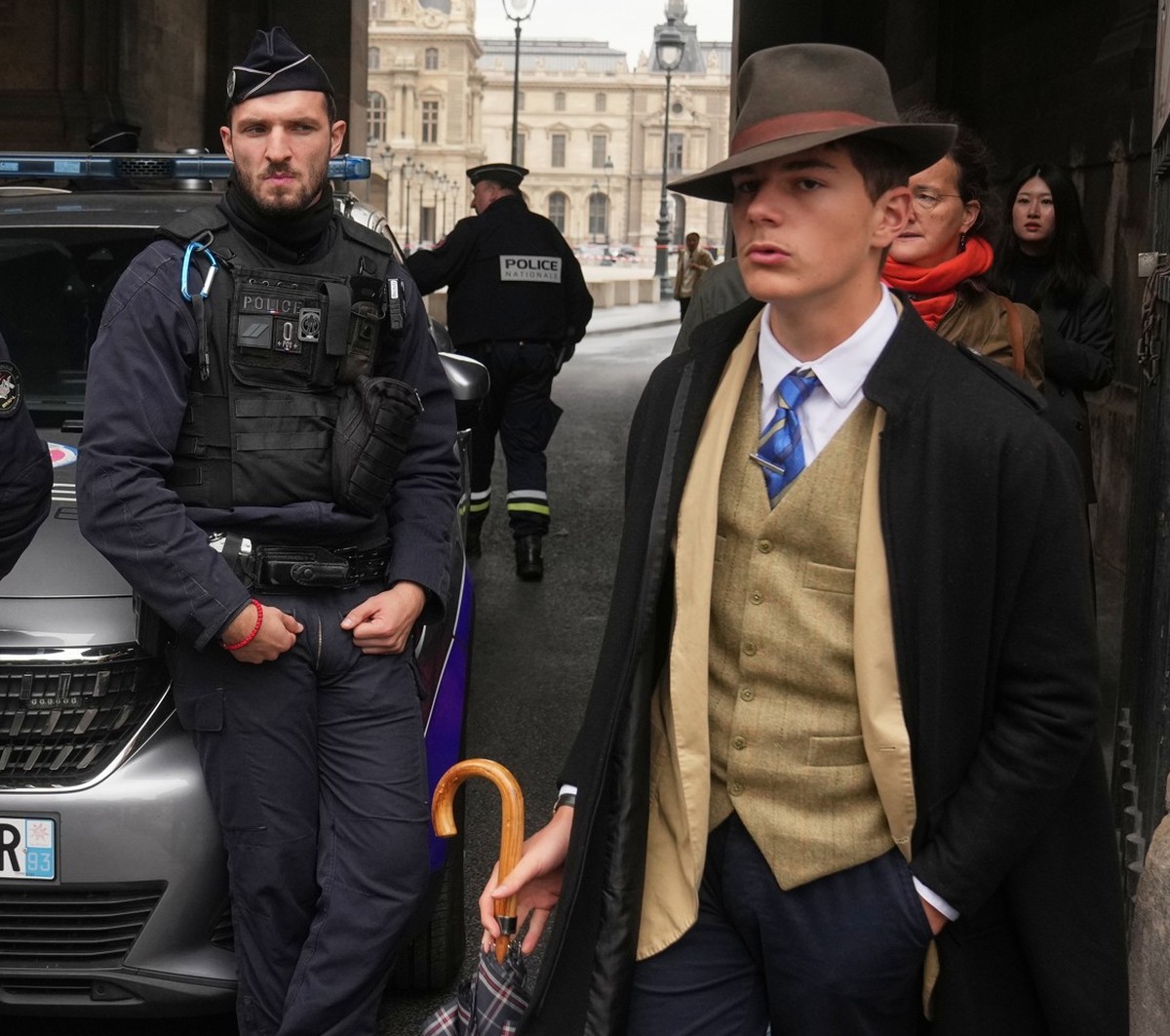 L'homme, vêtu d'un gilet boutonné, d'un trench-coat et d'un fedora, qui semblait surveiller la scène, a déclenché l'indignation sur Internet. (AP Photo/Thibault Camus)