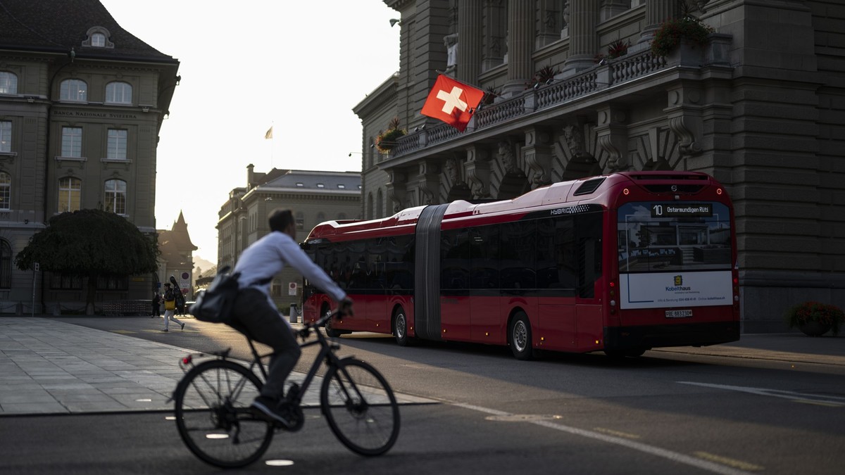 Die Schweizer Fahne am Parlamentsgebaeude leuchtet in der Morgensonne, waehrend ein Velofahrer und ein Bus von Bernmobil vorbeifahren, an der Herbstsession der Eidgenoessischen Raete, am Mittwoch, 11. ...