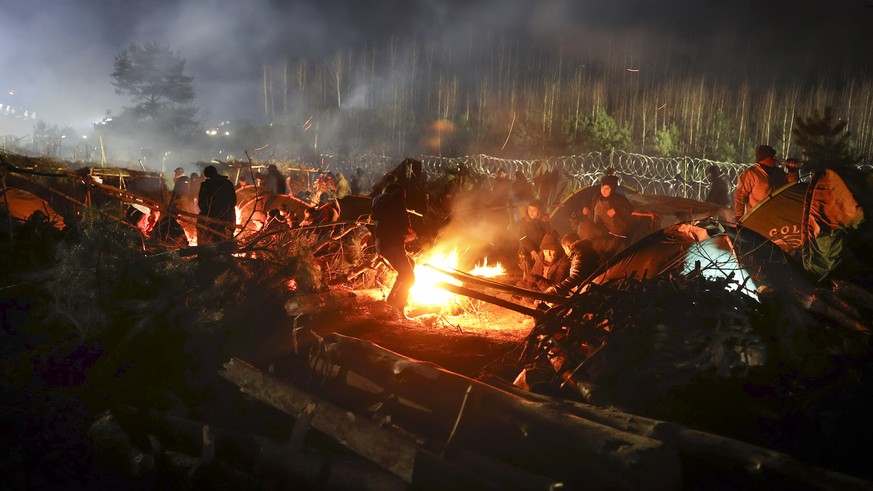 Migrants warm themselves at a fire in frigid conditions as they gather at the Belarus-Poland border near Grodno, Belarus, Saturday, Nov. 13, 2021. Belarusian state news agency Belta reported that Luka ...