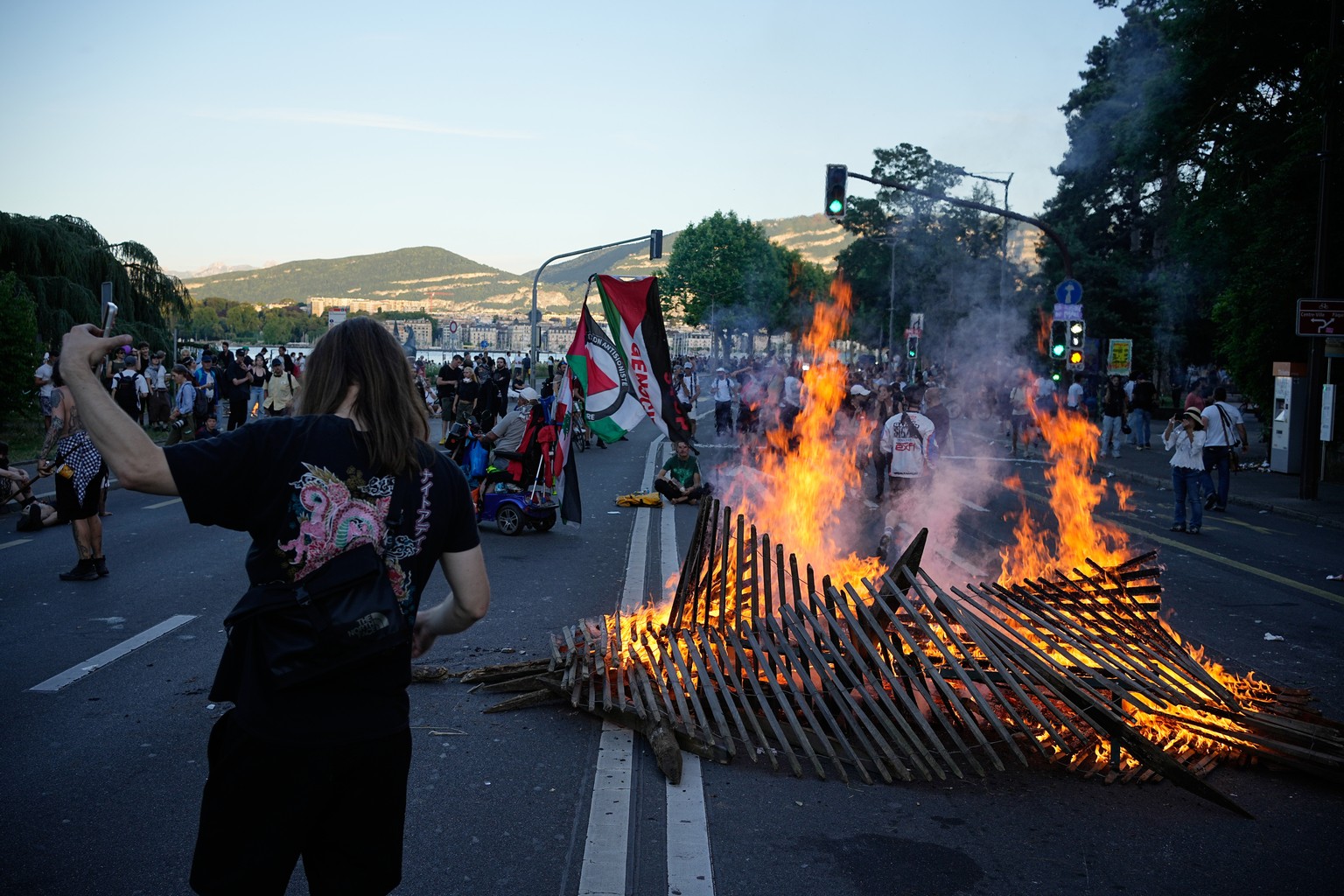 A protester walks as a fire burns in the street during a "No G7" demonstration in Geneva, Switzerland, Sunday, June 14, 2026, ahead of the G7 summit scheduled to take place June 15-17. (AP P ...