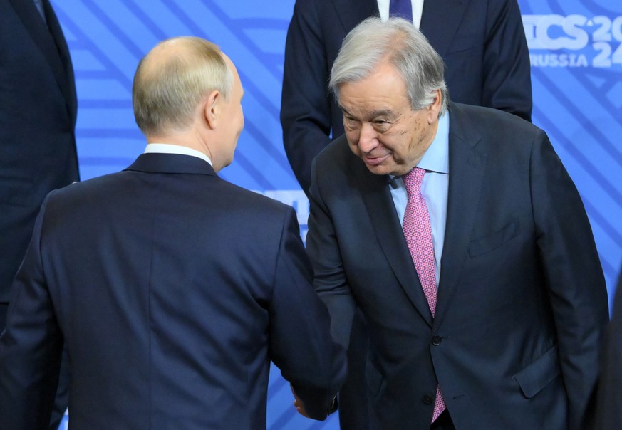 epa11679411 A handout photo made available by photo host brics-russia2024.ru shows Russian President Vladimir Putin (L) greeting United Nations Secretary-General Antonio Guterres (R) as other particip ...