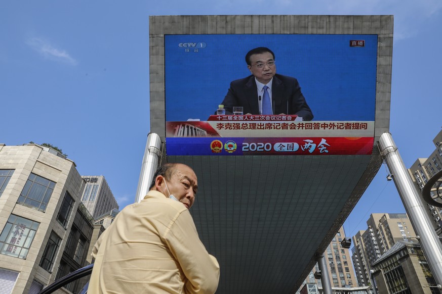 epa08449073 A man stands near a large screen displaying a press conference by Chinese Premier Li Keqiang following the closing ceremony of the third session of the 13th National People&#039;s Congress ...